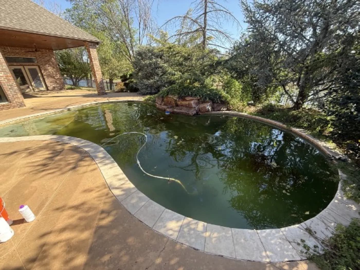 Green pool with a rock waterfall before algae treatment in the OKC area